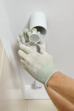 The worker is installing an LED spotlight on the ceiling. Stock Photos