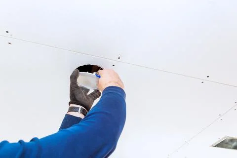 Worker installing lighting fixture in drywall ceiling during home renovation Stock Photos