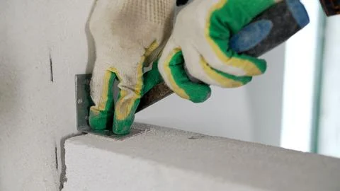 Worker installing metal bracket on concrete block wall with hammer and glov.. Fotos de archivo