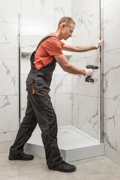 The worker is installing a metal profile of the shower cabin with a screwdriv Stock Photos