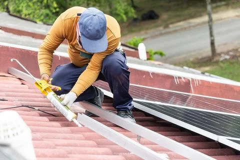 Worker installing mounting brackets onto red residential roof for solar Stock Photos