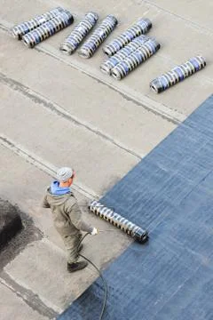 Worker installing roofing felt with heating and melting bitumen roll by torch on Stock Photos