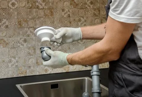 An worker is installing a sewer drain for the kitchen sink. Stock Photos