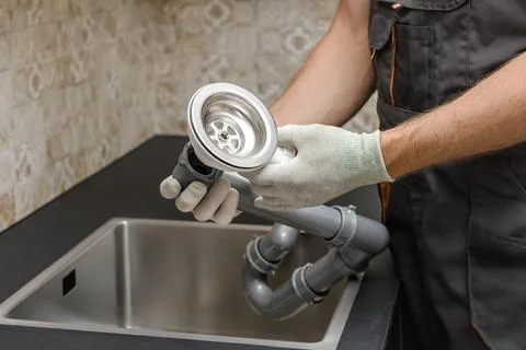 An worker is installing a sewer drain for the kitchen sink. Stock Photos