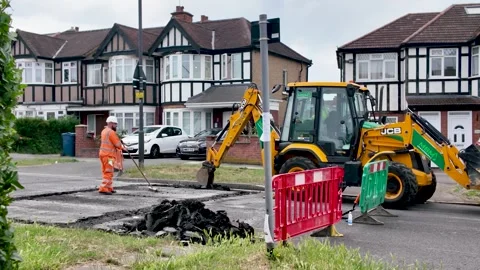 Worker installing speed bumps on a residential street with a JCB backhoe loader Stock Footage 336563949