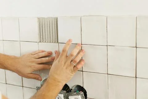 Worker installing stylish white tiles on wall at electricity socket. Hands .. Stock Photos