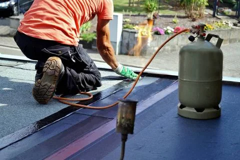 Worker installing tar foil on the rooftop of building. Flat roof installat... Fotos de archivo