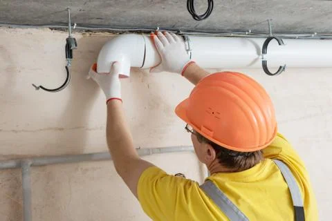 The worker is installing a ventilation system. Stock Photos