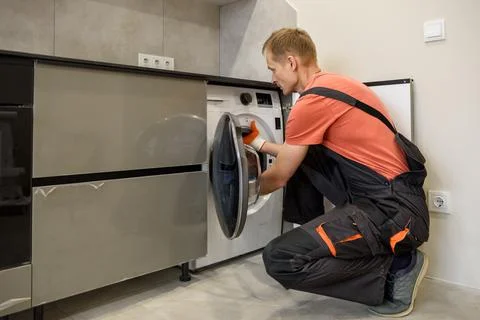 The worker is installing a washing machine in the kitchen furniture. Stock Photos