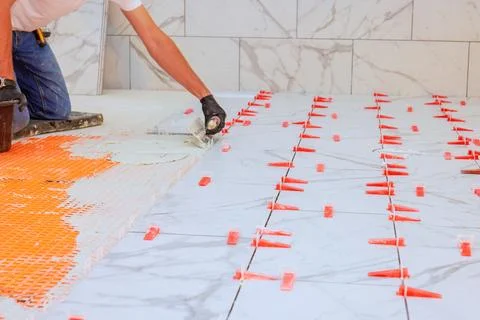 Worker installing white marble tiles on floor with careful attention to Stock Photos