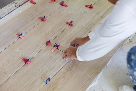 Worker installing wood look tile flooring using leveling system Stock Photos