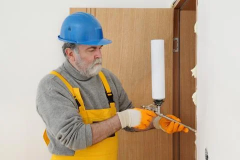 Worker installing wooden door, using polyurethane foam 库存照片