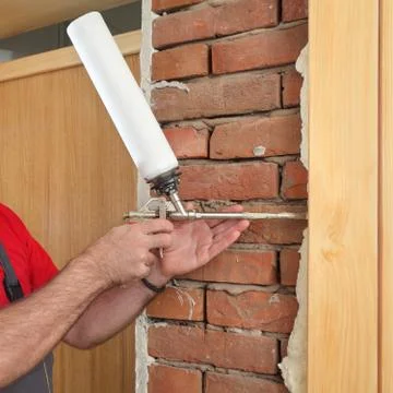 Worker installing wooden door, using polyurethane foam Stock Photos