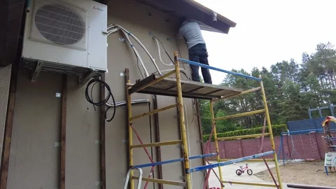 Worker installs air conditioning units on a building near a garden area with pla Stock Footage 340357203