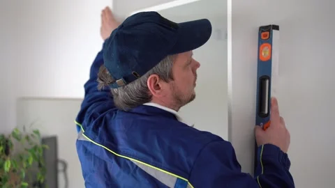 A worker installs a cabinet frame. man in uniform measure the wardrobe level Stock Footage 221814064