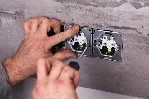 A worker installs an electrical outlet into a wall using a screwdriver Stock Photos