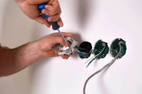 A worker installs an electrical outlet into a wall using a screwdriver Stock Photos