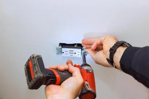 Worker installs electrical outlet on white celling using an electric screwd.. 스톡 사진