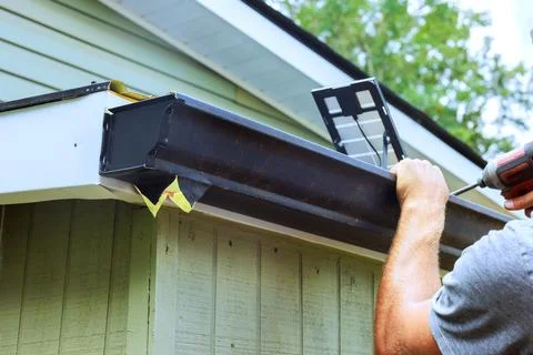 Worker installs gutter on building under clear skies Fotos de archivo