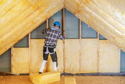 Worker installs insulation in attic during home renovation process Stock Photos