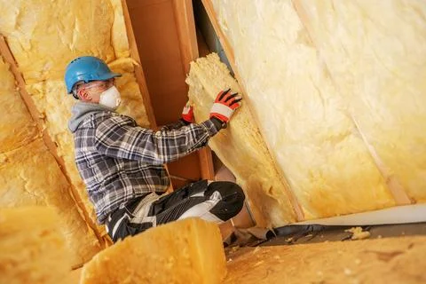 Worker installs insulation in a building under construction during the day Stock Photos