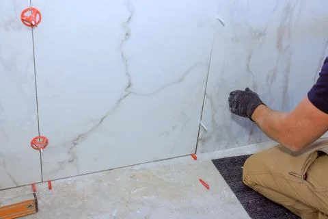 Worker installs large tiles on wall in construction area while using tools .. Stock Photos