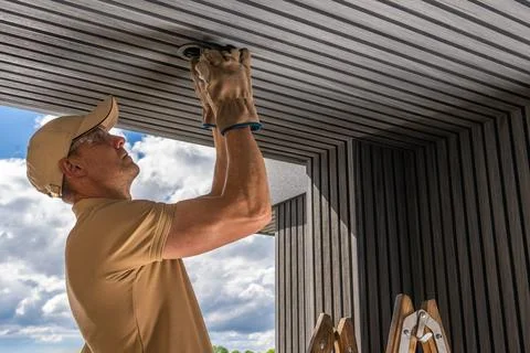 Worker installs lighting fixture on a ceiling during day at a construction si Foto stock