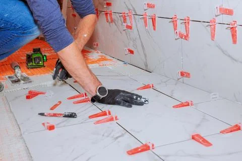 Worker installs marble tiles on floor with spacers in home renovation project Stock Photos