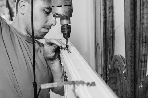 A worker installs new plastic windows in the house, drills holes in the window Stock Photos