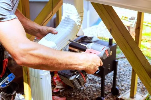 Worker installs section of gutter at home site Stock Photos