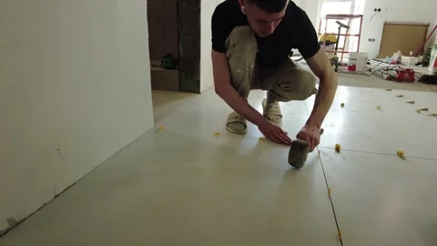 Worker installs tiles on a floor using tools and materials in a construction sit Stock Footage 332473555