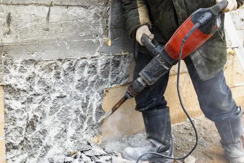 A worker with a jackhammer at a construction site levels a concrete wall. Photos