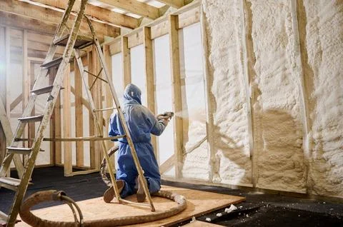 Worker kneeling and spraying polyurethane foam insulation into wall cavity .. Stock Photos