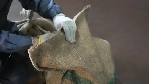 Worker kneels beside a burlap sack securing a bundle of chains with wire and Stock Footage 339128685
