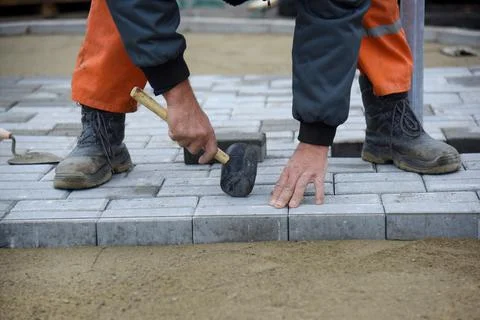 A worker knocks with a hammer, levels the paving slabs. Stock Photos