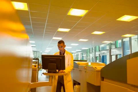 Worker in lab coat at computer among printers in printing plant Stock Photos