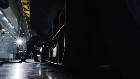 Worker Laboring Under Large Boat Hull, Dark Shipyard Hall, Backlit Silhouette Vídeo Stock 340329625
