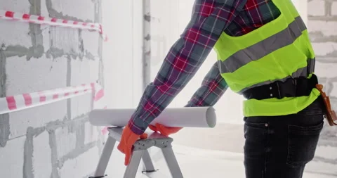 Worker with ladder approaches work area and unfolds floor plan Stockbeeldmateriaal 309084947