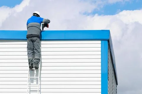 Worker on Ladder Installing Equipment on Building Roof Stock Photos
