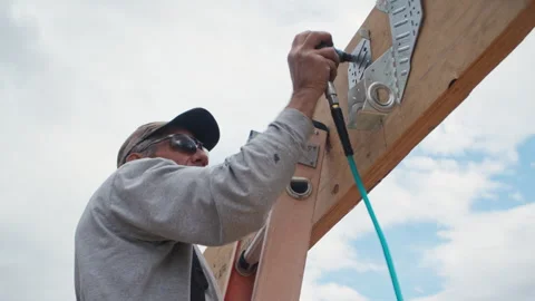 Worker on a ladder uses a pneumatic palm nailer to nail in supports. Stock Footage 305668650