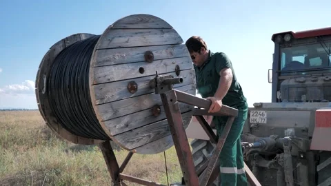 Worker lay the cable in the ground with a large wheeled tractor Stock Footage 248070489