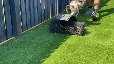 Worker laying artificial grass in backyard, aligning and stretching turf. Stock Photos