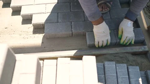 Worker laying gray paving stones on sandy base under bright sunlight Stock Footage 337995366