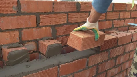 The worker lays the brick on a pre-prepared layer of cement mortar. Construction Stock Footage 157345697