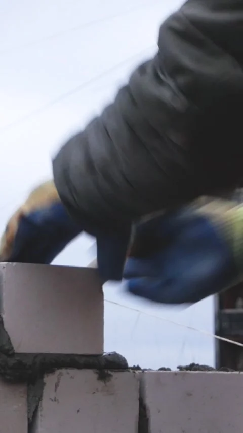 A worker lays bricks on cement, builds the wall of the house Stock Footage 311976025