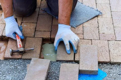 Worker lays bricks on pathway during patio pavement repair with hammer Stock Photos