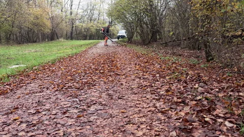 A worker with leaf blower cleans up autumn leaves to clear the cycle path. Stock Footage 295811130