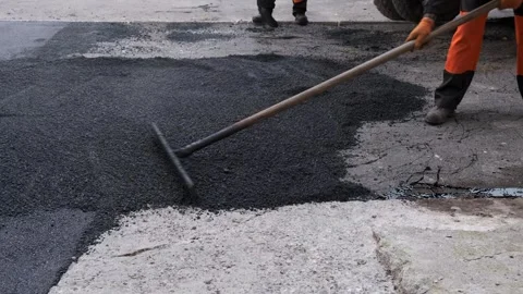 Worker leveling hot fresh black asphalt on a street using a metal rake Vídeos de archivo 339801851