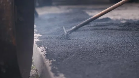 Worker leveling steaming hot black asphalt with a metal rake tool on sidewalk Stock Footage 339801949