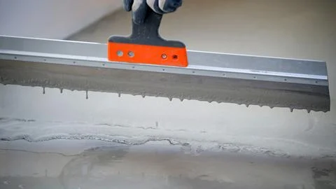 Worker levels concrete using a trowel at a construction site during day hours Photos